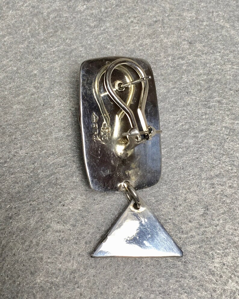 May include: Silver dangle earrings with a rectangular top and a triangular dangle. The earrings have a silver hook closure.