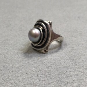 Peut inclure: Une bague en argent avec une perle grise sertie dans un motif tourbillonnant et concentrique.