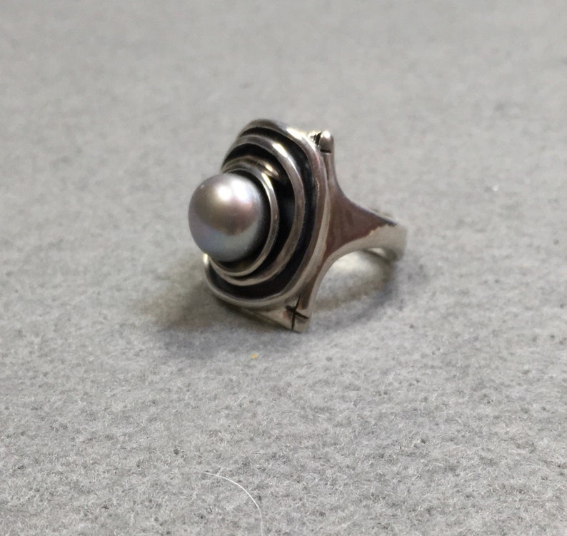 Peut inclure: Une bague en argent avec une perle grise sertie dans un motif tourbillonnant et concentrique.