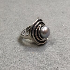 Peut inclure: Une bague en argent avec un motif en spirale et une perle grise au centre.