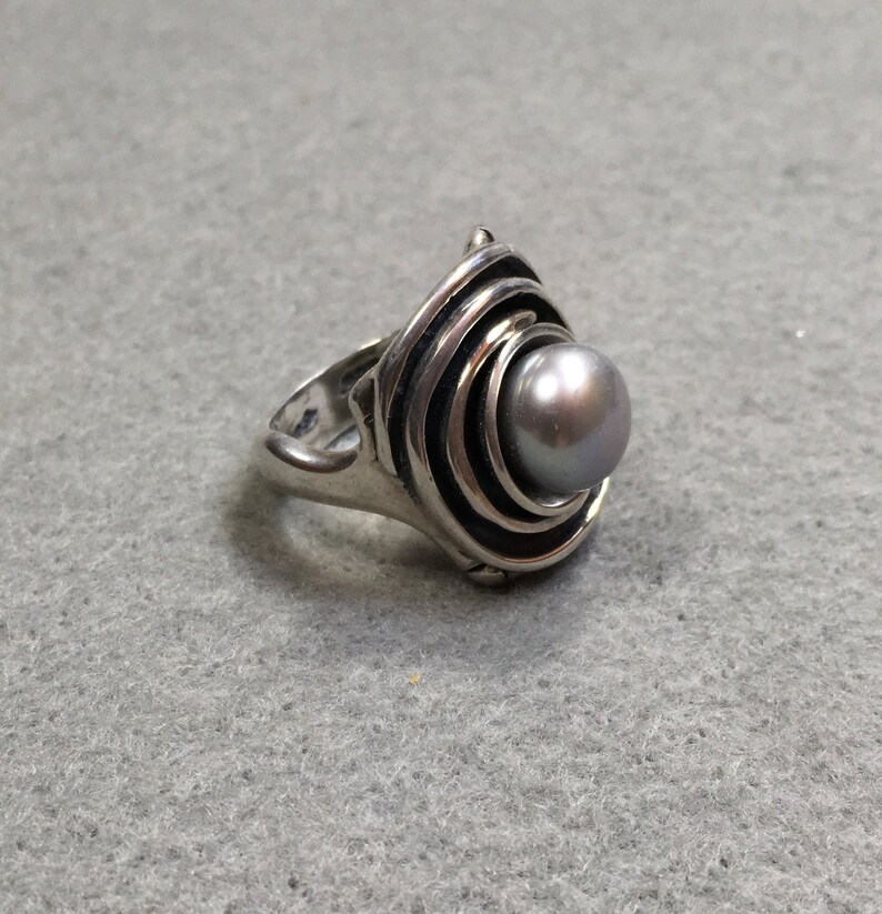 Peut inclure: Une bague en argent avec un motif en spirale et une perle grise au centre.