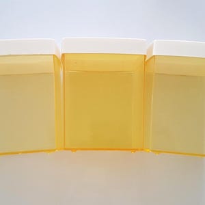 May include: Three translucent yellow plastic containers with white lids are arranged side by side. The containers are rectangular with a slightly tapered design. The image is taken against a white background.
