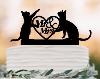 Op de afbeelding: Zwarte silhouet van twee katten die een hart vasthouden met "Mr & Mrs" erop. De topper staat op een witte bruidstaart.