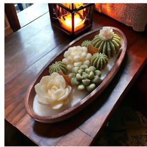 May include: A wooden oval tray with six succulent-shaped candles. The candles are in shades of green and white. The tray is on a wooden table.
