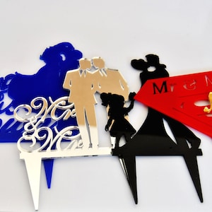 May include: Four different cake toppers made of acrylic. The first topper is blue with the text "Mr & Mrs Brown". The second topper is silver with the text "Mr & Mrs". The third topper is black with a couple dancing and the text "Mr & Mrs". The fourth topper is gold with a couple dancing and the text "Mr & Mrs".