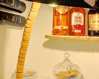 May include: A distinctive lamp featuring a black hat-shaped shade. The lamp's stem is made from stacked, circular pieces, and it sits on a rectangular base. A glass container and bottles of liquor are visible in the background.