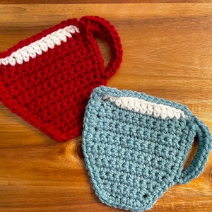 May include: Two crocheted cup coasters, one red with a white rim and one teal with a white rim.
