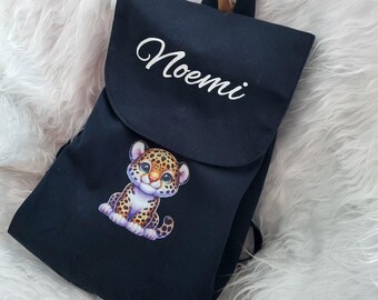 Könnte beinhalten: Schwarzer Canvas-Rucksack mit einem weißen gestickten Namen "Noemi" und einem Cartoon-Leopardenmuster. Der Rucksack hat verstellbare Träger.