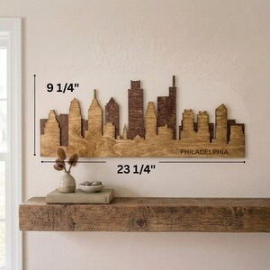 Puede incluir: Arte mural de madera con la silueta de Filadelfia, que mide 59 cm de ancho y 23,5 cm de alto. La silueta est&aacute; cortada con l&aacute;ser en madera, con un dise&ntilde;o marr&oacute;n de dos tonos. La palabra "PHILADELPHIA" est&aacute; grabada en la parte inferior.