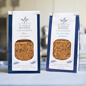 May include: Two packages of Norwegian baked knäckebröd crispbread, one labeled "Classic" and the other "Sea Salt Flakes." The packaging is white with blue accents and features a wheat sprig design. Each package contains 8 oz (227g) of crispbread.