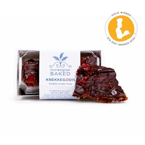 May include: A rectangular clear plastic container holds Norwegian Baked KNEKKEGODIS, a dark chocolate-covered crisp topped with red dried fruit pieces. A white paper label features blue text and a wheat graphic, plus a gold SFA Sofi Awards 2026 seal.