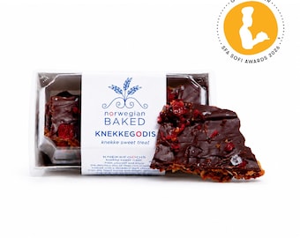 May include: A rectangular clear plastic container holds Norwegian Baked KNEKKEGODIS, a dark chocolate-covered crisp topped with red dried fruit pieces. A white paper label features blue text and a wheat graphic, plus a gold SFA Sofi Awards 2026 seal.