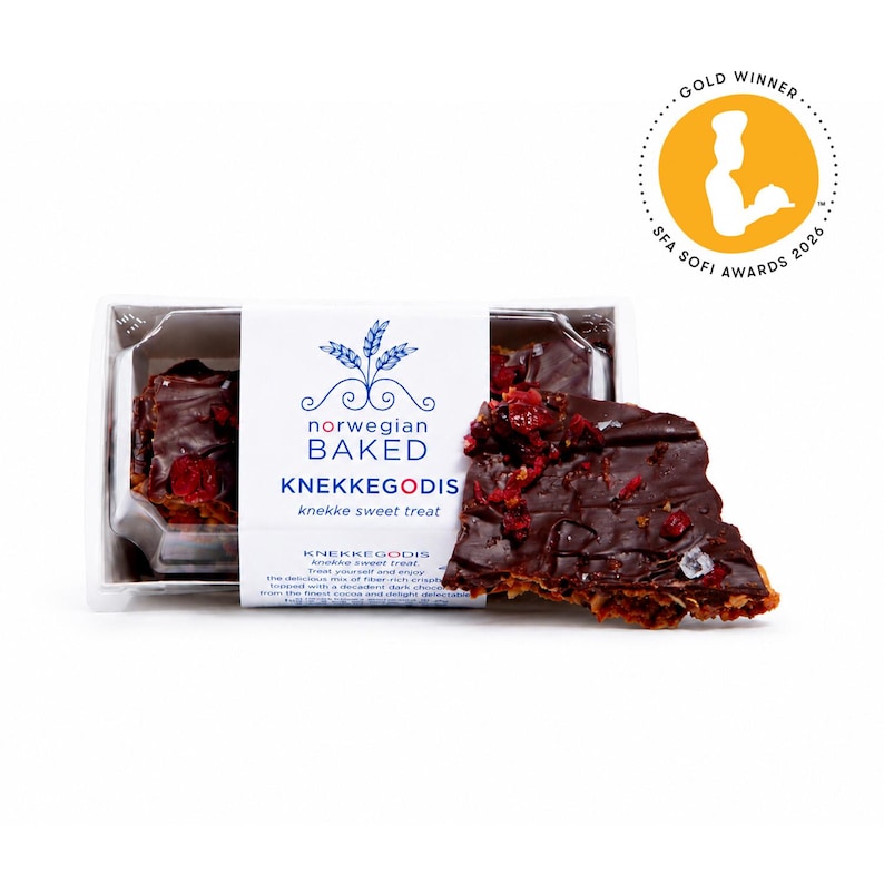 May include: A rectangular clear plastic container holds Norwegian Baked KNEKKEGODIS, a dark chocolate-covered crisp topped with red dried fruit pieces. A white paper label features blue text and a wheat graphic, plus a gold SFA Sofi Awards 2026 seal.