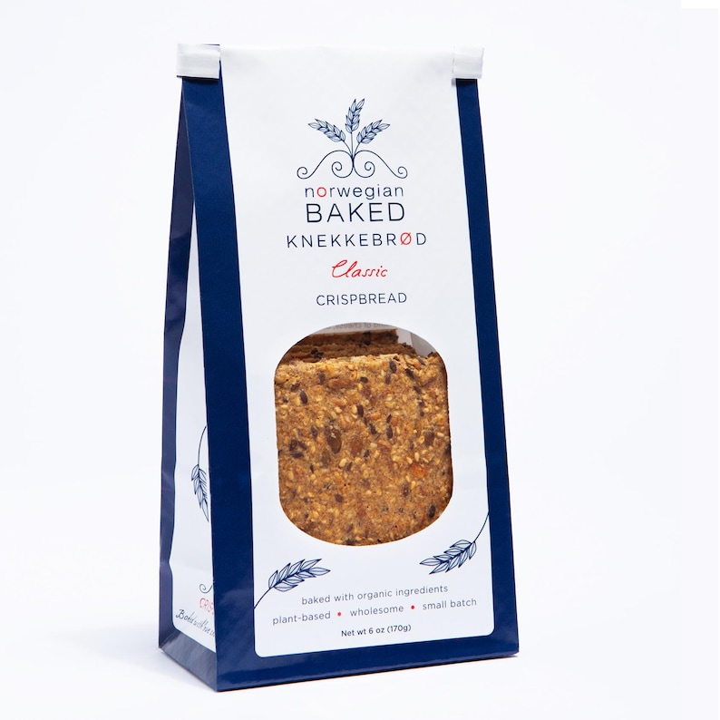 May include: A white and dark blue bag of Norwegian Baked Knekkebr&oslash;d Classic crispbread. The packaging features a circular window revealing the textured, seed-filled crackers inside. Text includes "norwegian BAKED KNEKKEBR&Oslash;D" and "Net wt 6 oz (170g)".