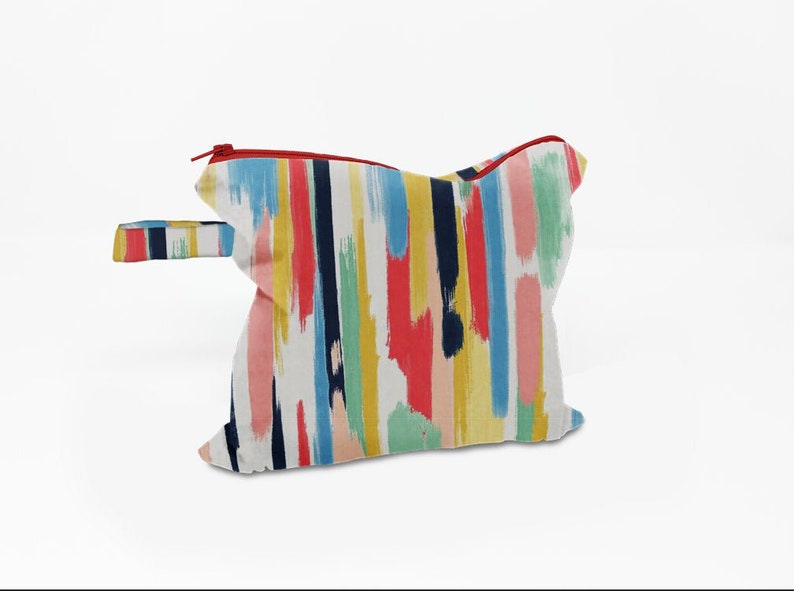 May include: A colourful zippered pouch with a white background and abstract brushstroke patterns in shades of blue, yellow, red, pink, and green. The pouch has a red zipper and a black handle.
