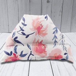 Puede incluir: Una almohada blanca con un patrón floral en tonos de rosa y azul. La almohada tiene forma de triángulo y tiene una costura en el medio.