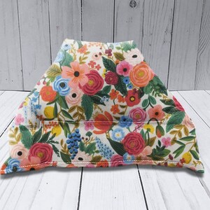 Puede incluir: Una almohada de tela de forma triangular, de color crema, con un patr&oacute;n floral en tonos de rosa, rojo, azul, verde y amarillo. La almohada est&aacute; rellena de relleno y tiene una costura en el centro.