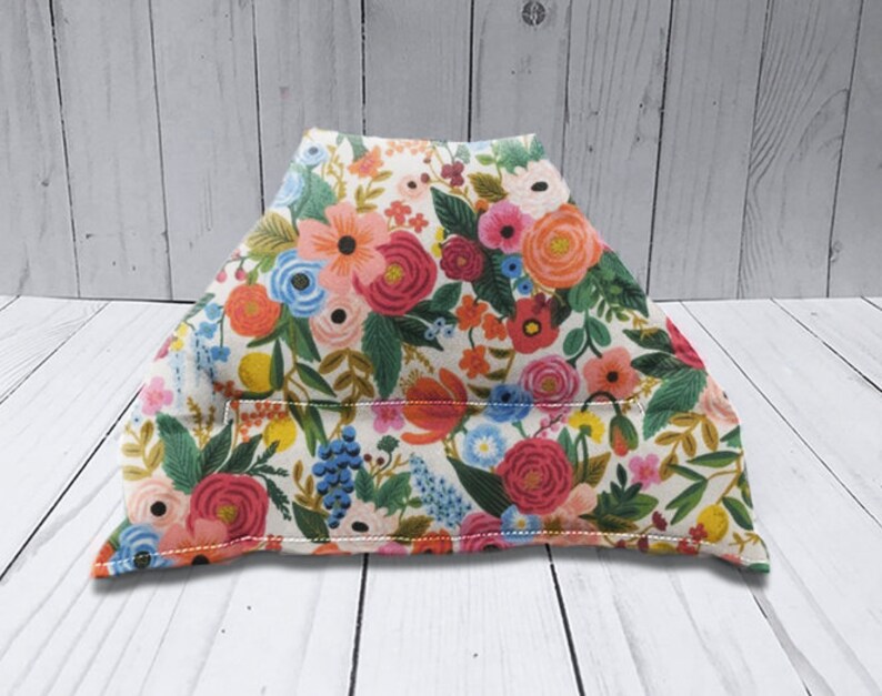 Puede incluir: Una almohada de tela de forma triangular, de color crema, con un patr&oacute;n floral en tonos de rosa, rojo, azul, verde y amarillo. La almohada est&aacute; rellena de relleno y tiene una costura en el centro.