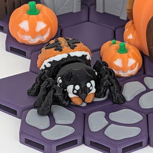 May include: A Halloween-themed display featuring a black and white spider with an orange pumpkin head, surrounded by orange pumpkins and purple hexagonal tiles. The scene includes gray tombstones, creating a spooky atmosphere.