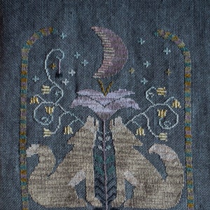 Puede incluir: Bordado con dos lobos aullando a una luna creciente con una flor y enredaderas. El texto "Sing to the Moon" está debajo de los lobos.