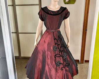 May include: A maroon taffeta dress with a black velvet trim and a black floral design with pearl accents. The dress has a fitted bodice and a full skirt.