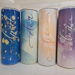 May include: Four personalized stainless steel tumblers with different designs and names. The tumblers are blue, green, orange, and purple with white lettering. The names are April, Ana, Kihm, and Amy.