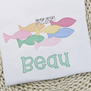 May include: A white onesie with a green embroidered name "Beau" and a design of five colorful fish swimming in a row.