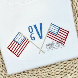 May include: White t-shirt with embroidered American flags crossed over each other. The letters "OG" and "V" are embroidered in blue and white above the flags. The text "Simple Sweet Mama" is embroidered below the flags.