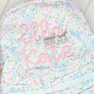 May include: A pink and white floral print backpack with the names "Ella Kate" embroidered in pink on the front. The text "Simple Sweet Mama" is also embroidered in pink on the front.