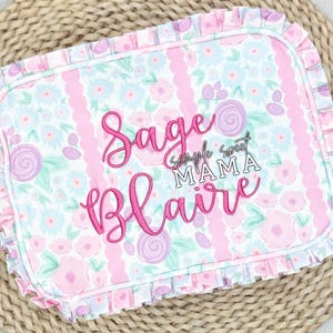 May include: A rectangular baby blanket with a floral pattern in pink, blue, and purple. The blanket features the names "Sage" and "Blaire" embroidered in pink script, with "Simple Sweet MAMA" in silver lettering. The edges are trimmed with a ruffled border.