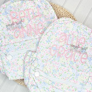 May include: Two floral print backpacks with personalized embroidery. The first backpack says "Beth Anne Mama" and the second backpack says "Allie Grace Mama".