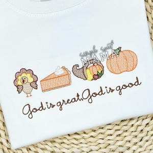 May include: Embroidered design on a white t-shirt featuring a turkey, pumpkin pie, cornucopia, and the text "God is great. God is good."