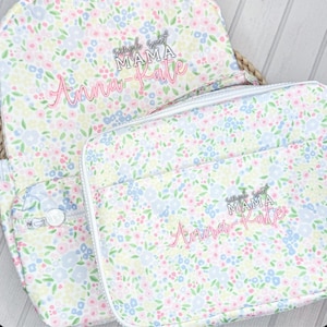 May include: A floral print backpack and matching lunch bag. The pattern features small pink, blue, and yellow flowers on a white background. The backpack and lunch bag have the text "Simple Sweet Mama Anna-Kate" in pink script.