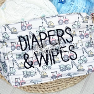 May include: A white diaper bag with a pattern of construction vehicles in pastel colors. The bag has the words "DIAPERS & WIPES" embroidered in black. The bag is sitting in a woven basket.