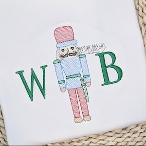 May include: Embroidered design featuring a green "W" and "B" with a red, blue, and green nutcracker in the center.
