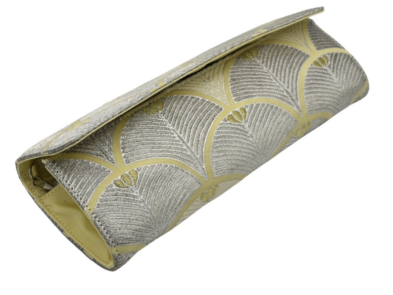 May include: A light yellow clutch bag with a silver and gold geometric pattern.