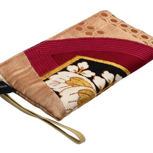 K&ouml;nnte beinhalten: Eine kleine, beige, rosa und schwarze Stofftasche mit Blumenmuster und einem goldenen Riemen. Die Tasche hat ein schwarzes Etikett mit der Aufschrift "ANNIKA".