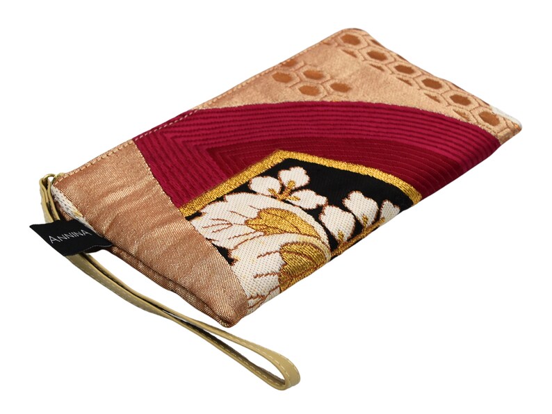 K&ouml;nnte beinhalten: Eine kleine, beige, rosa und schwarze Stofftasche mit Blumenmuster und einem goldenen Riemen. Die Tasche hat ein schwarzes Etikett mit der Aufschrift "ANNIKA".