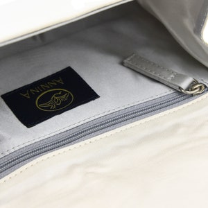 May include: A white leather purse with a zippered pocket and a black label that says "ANNINA" with a gold bird logo.