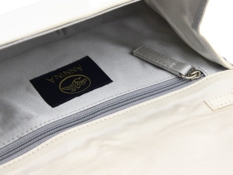 May include: A white leather purse with a zippered pocket and a black label that says "ANNINA" with a gold bird logo.