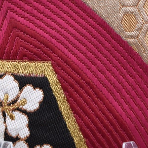 K&ouml;nnte beinhalten: Nahaufnahme eines Stoffes mit einem roten, goldenen und wei&szlig;en Muster. Der Stoff hat eine strukturierte Oberfl&auml;che und ist mit Blumen bestickt.