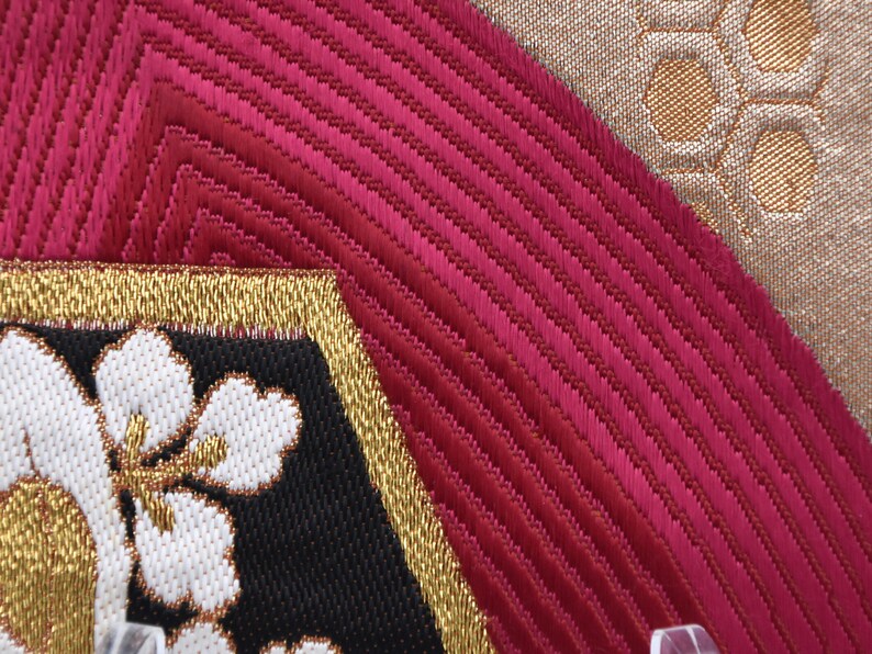 K&ouml;nnte beinhalten: Nahaufnahme eines Stoffes mit einem roten, goldenen und wei&szlig;en Muster. Der Stoff hat eine strukturierte Oberfl&auml;che und ist mit Blumen bestickt.