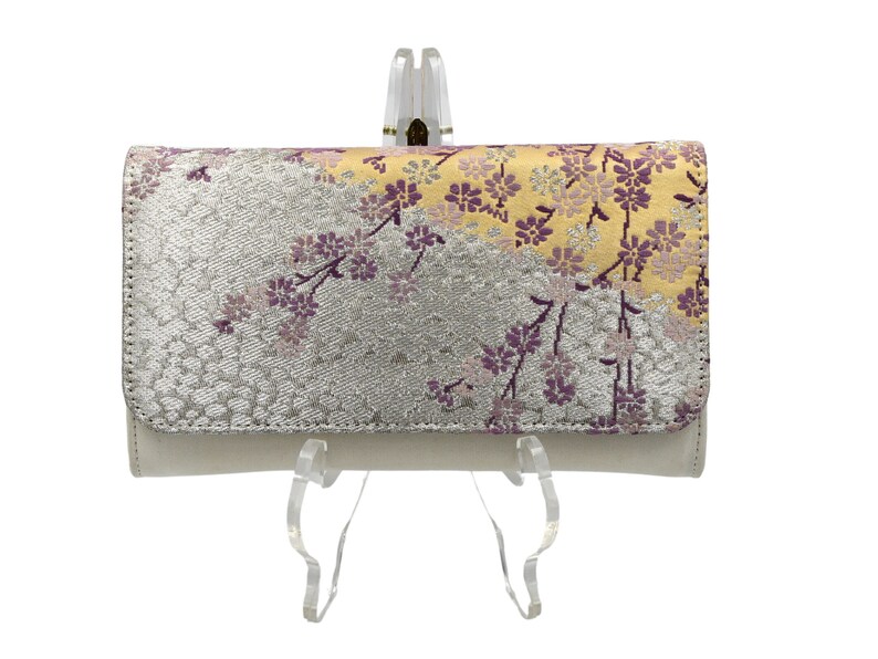 May include: A white wallet with a floral pattern in shades of purple, yellow, and silver. The wallet is on a clear stand.
