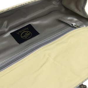 May include: A light beige clutch bag with a zip fastening and a silver metal logo that reads "ANNINA" in gold lettering.