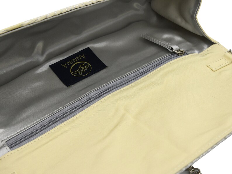 May include: A light beige clutch bag with a zip fastening and a silver metal logo that reads "ANNINA" in gold lettering.
