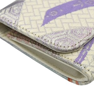 Puede incluir: Primer plano de una cartera de tela blanca y morada con un patr&oacute;n geom&eacute;trico. La cartera est&aacute; doblada y las costuras son visibles.