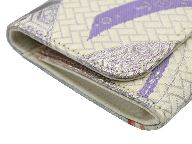 Puede incluir: Primer plano de una cartera de tela blanca y morada con un patr&oacute;n geom&eacute;trico. La cartera est&aacute; doblada y las costuras son visibles.