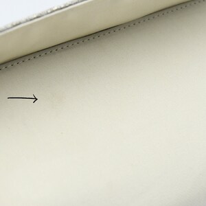 May include: The inside of a white clutch bag with a silver chain. The lining is white and has a small, faint stain.