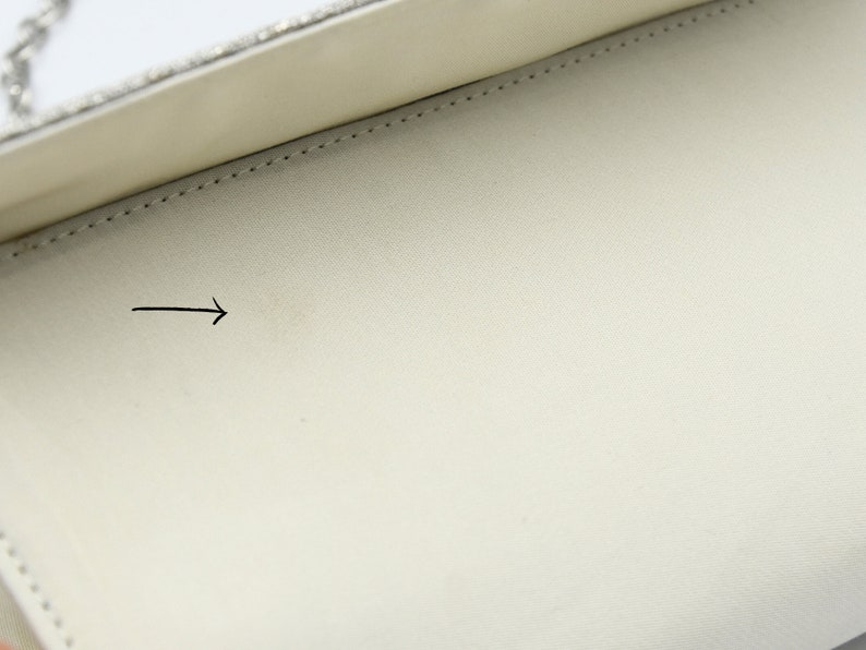 May include: The inside of a white clutch bag with a silver chain. The lining is white and has a small, faint stain.