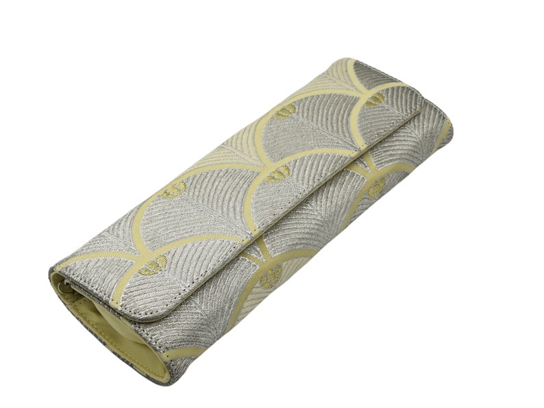 May include: A silver and yellow clutch bag with a geometric pattern. The bag is closed and has a flap.